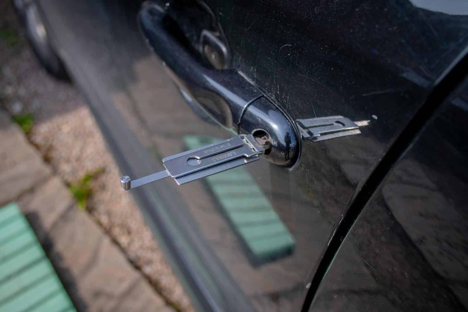 Close-up of a locksmith tool inserted into a car door lock, demonstrating security access.