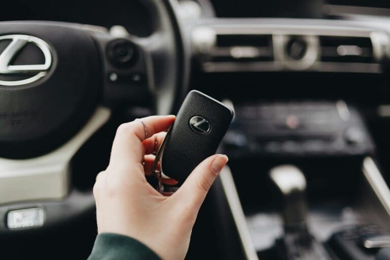 Person holding a Lexus car key inside a luxury vehicle's interior, showcasing brand elegance.